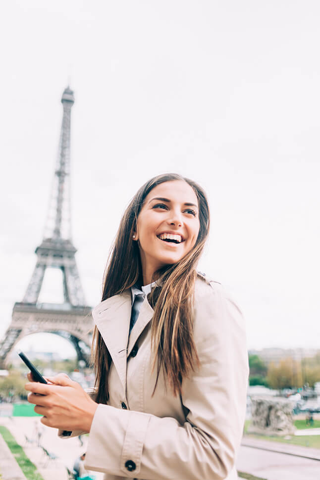 Woman in a beige trench coat standing in front of the Eiffel Tower in Paris.