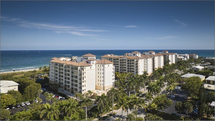 Ocean front resort with palm trees lining the roadway and blue skies above.