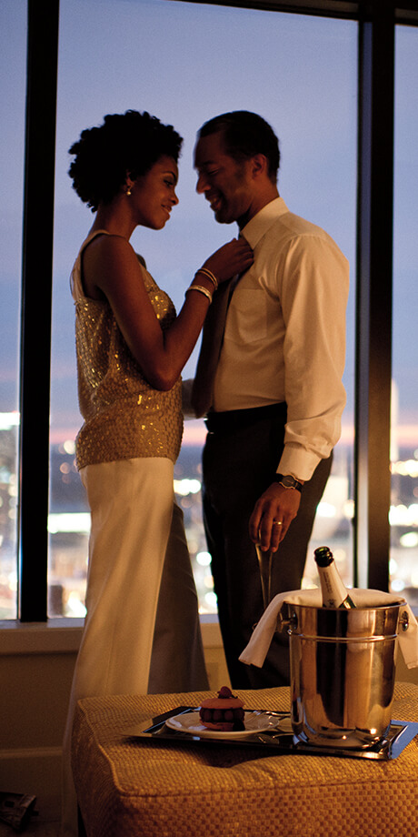 Couple standing by a window with a lit up skyline in the background