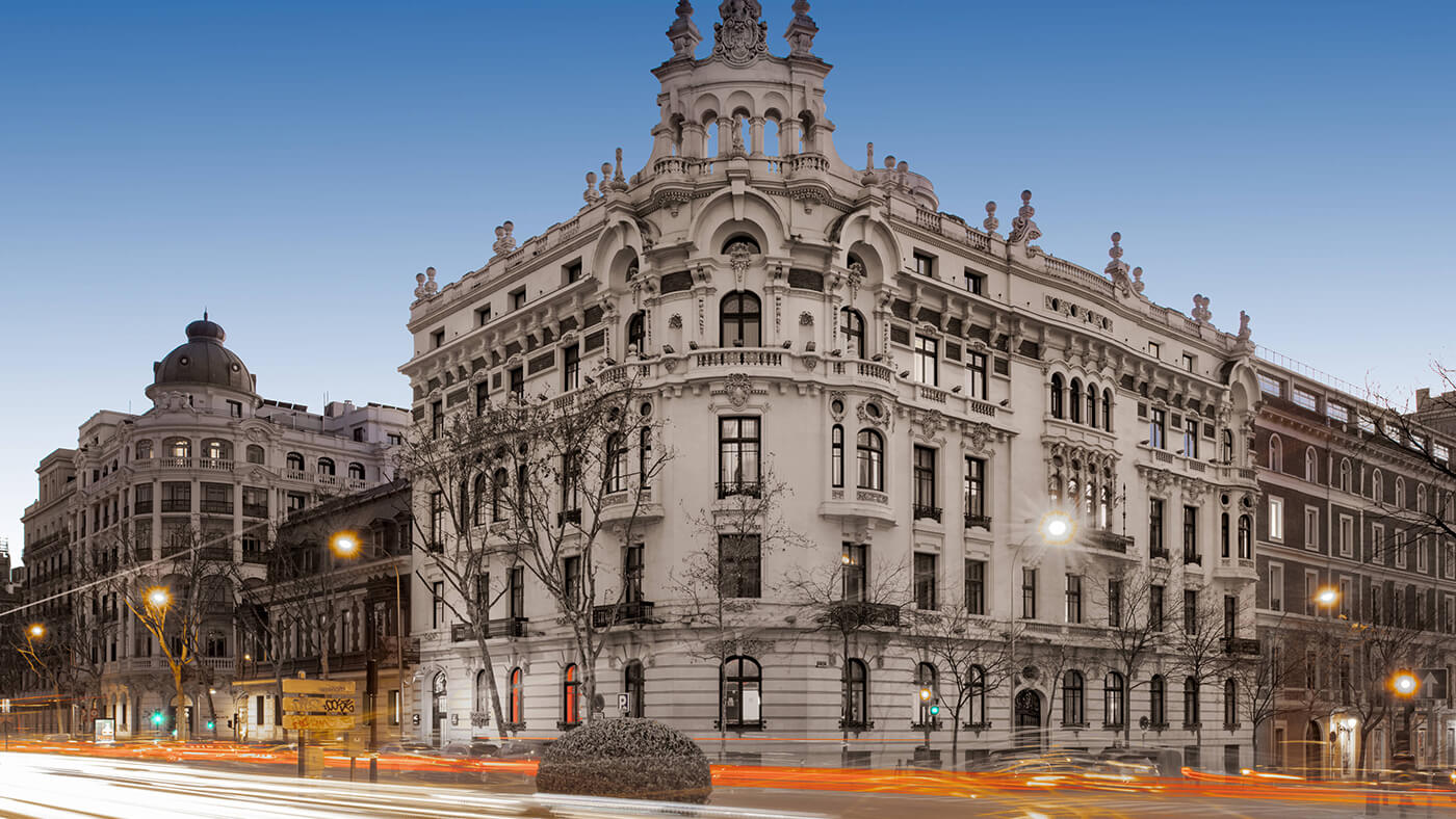 Corner exterior picture of Palacio del Retiro at sunset with lights from traffic whizzing by.