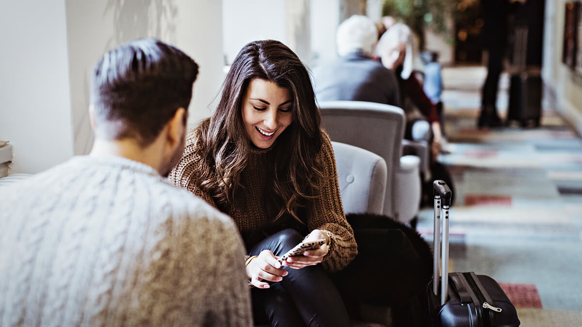 Woman sitting on a gray tufted chair looking at a mobile device and smiling