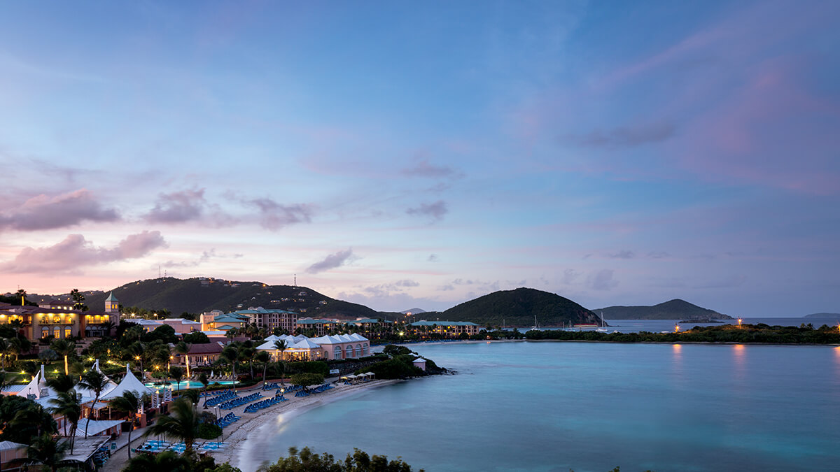 Image of a coastal resort at dusk with water and mountains.