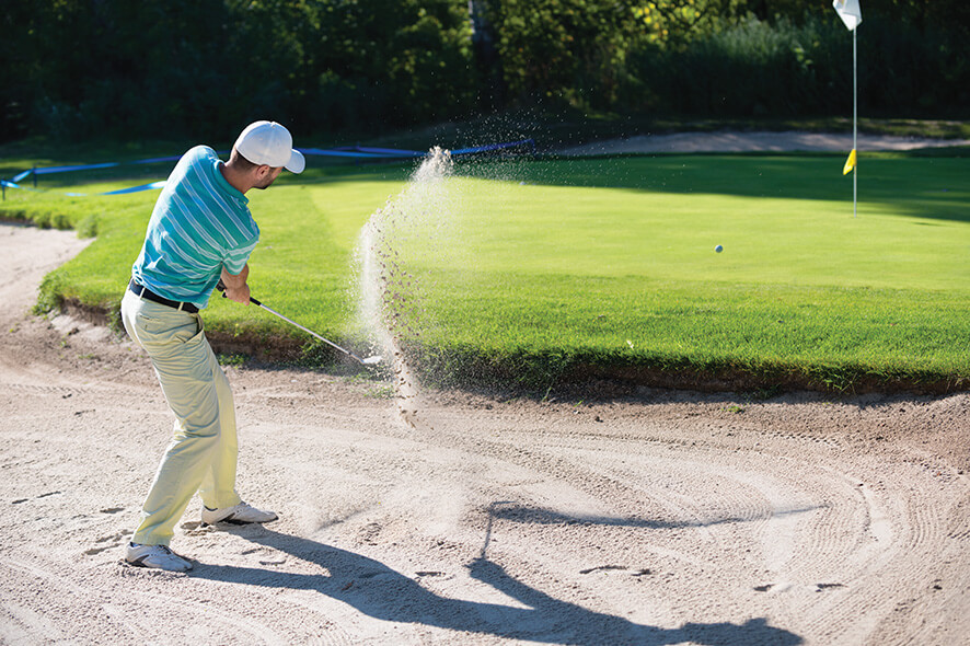 Golfer swinging the golf club out of the sand