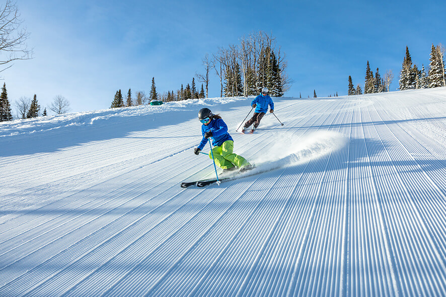 Skiers going down the slope in blue jackets with the blue skies above. 