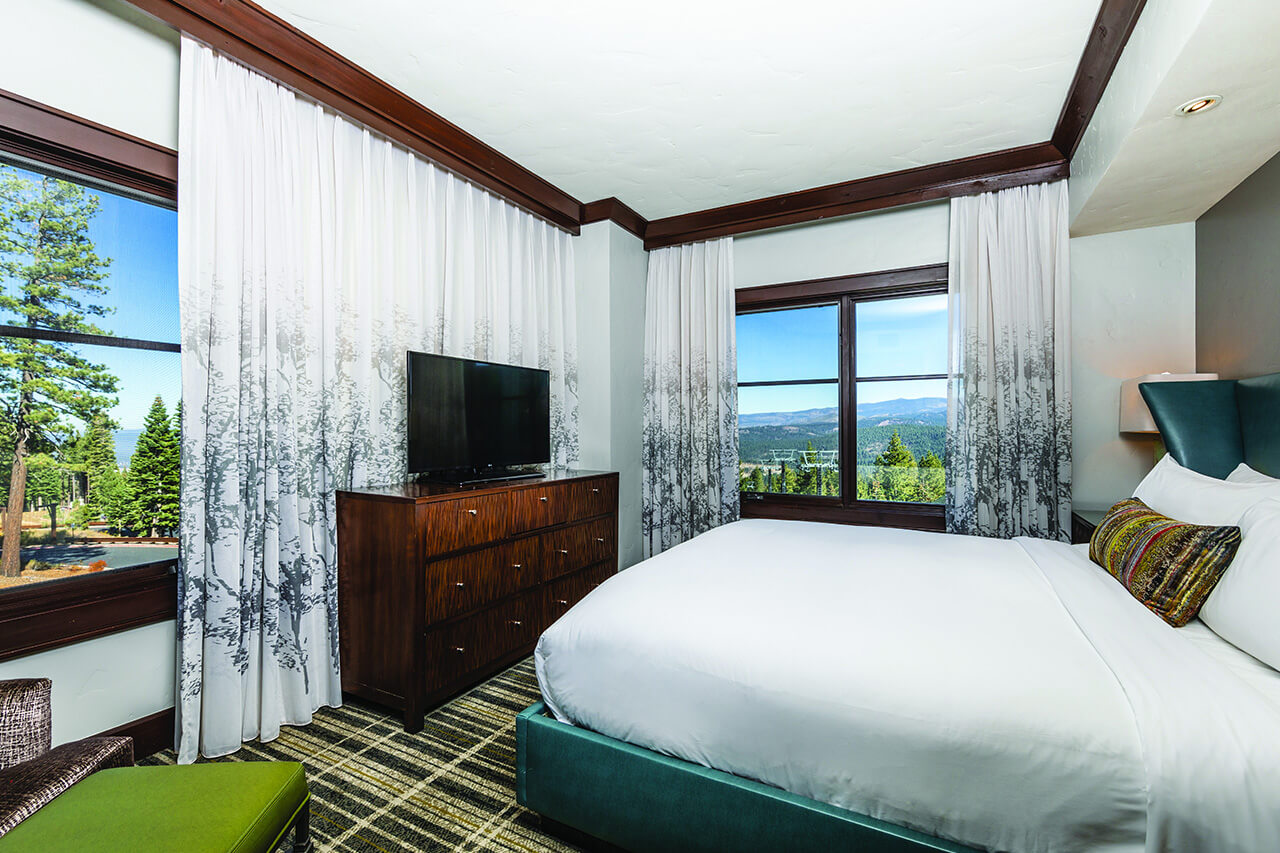 Bedroom with blue leather bed and white linens, plaid carpet and a dresser with a flat-screen tv.