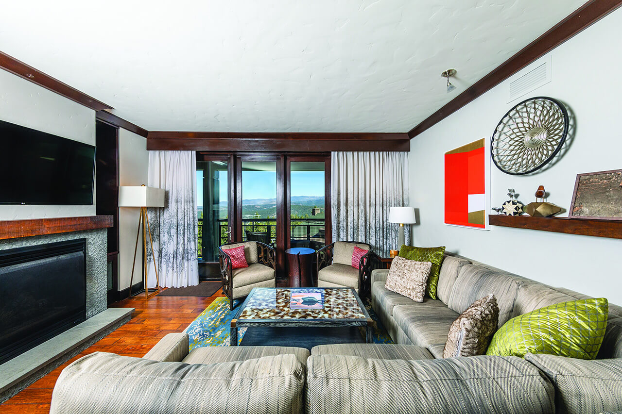 Living room in a residence at Ritz Carlton Club, Lake Tahoe, with a comfy sectional, neutral colored fabrics, fireplace, flat-screen tv, and a view of the mountains through the floor-to-ceiling sliders.