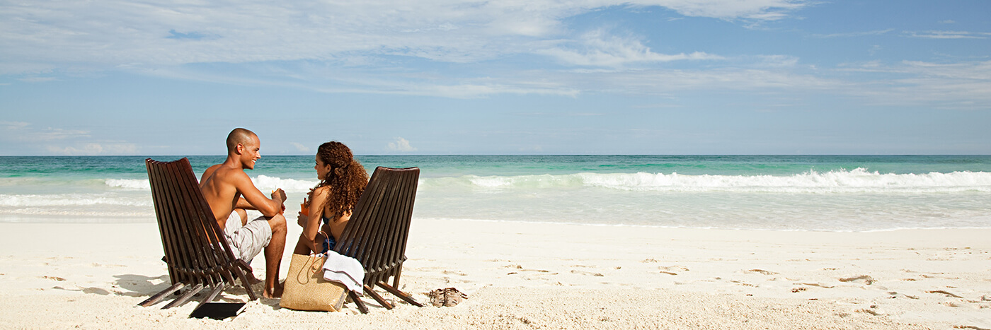 Couple sitting in wood chairs on a remote beach with waves crashing in front of them.