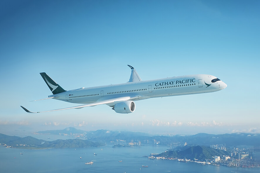 Cathay Pacific airplane flying in the air with ocean and mountains in the background.