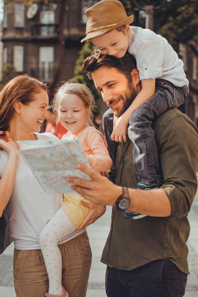 Two adults holding children smiling and looking at a travel map on the street