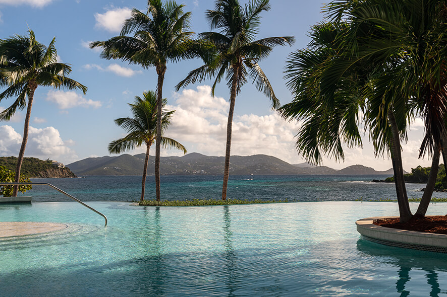 Free form outdoor pool with sparkling turquoise water surrounded by palm trees and the waters and mountains of St. Thomas