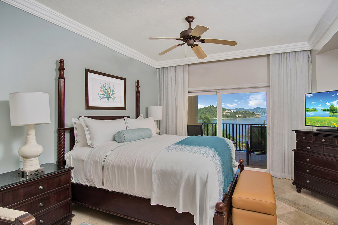 Tropical resort bedroom with a water view featuring a wood four-poster bed made with white linens and blue accents.