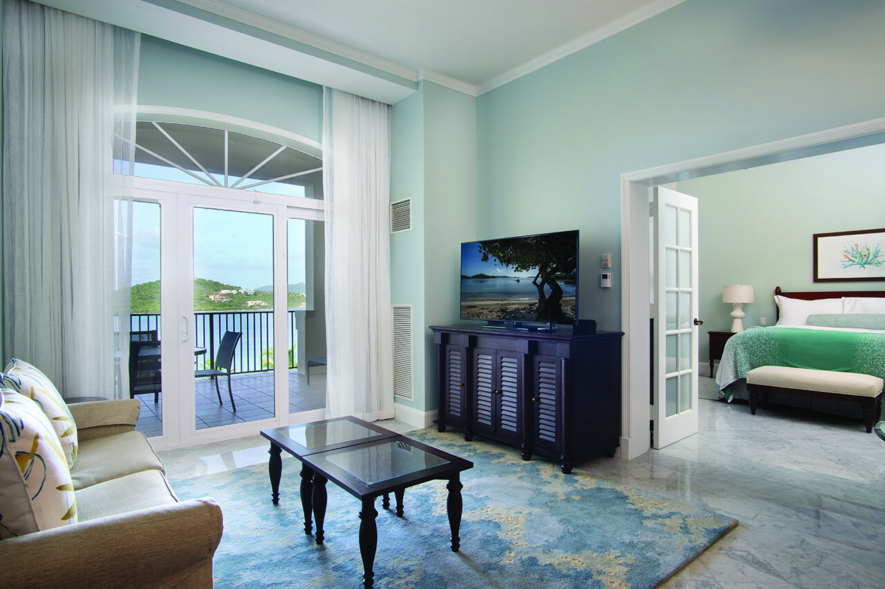 Resort living room with balcony and water views and an open door to the primary bedroom.