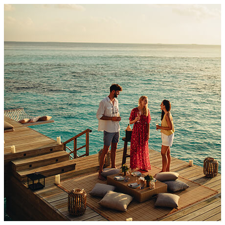 People at the seaside drinking wine on a wood deck with pillows and lanterns overlooking the water 