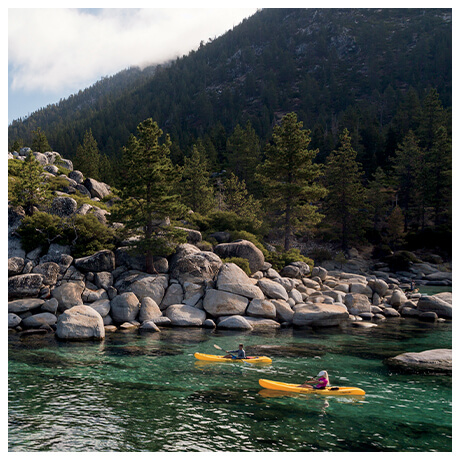 Two people in yellow kayaks on a boulder lined river