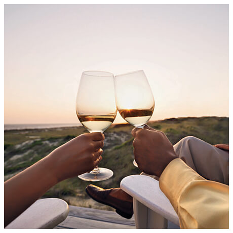 Holding wine glasses at sunset toasting.