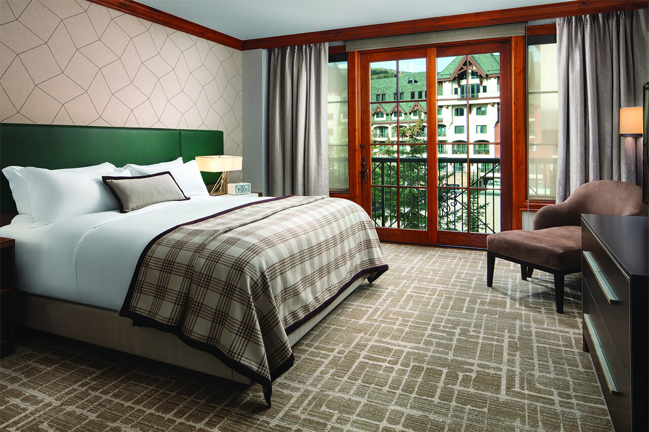 Kind bed in bedroom of resort with gray plaid and white linens and an emerald green headboard