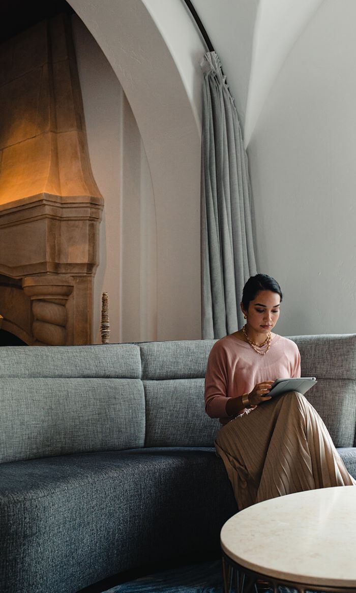 Woman sitting on a gray couch looking at her tablet device.