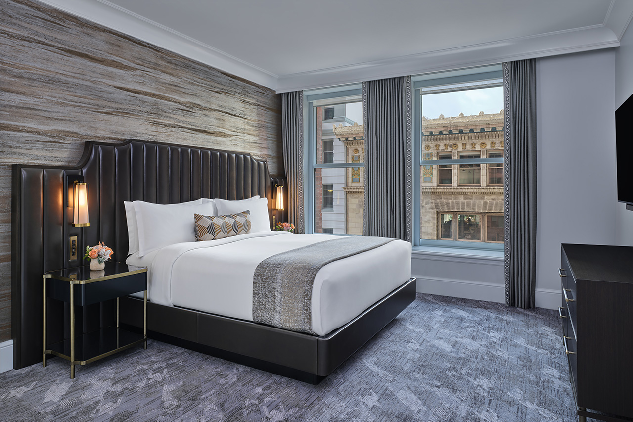 The Ritz-Carlton Club, San Francisco bedroom in a 1-bedroom residence. Furnished with a brown leather channel oversized headboard and bed, nightstands with lamps, dresser with flat-screen television, and views of the city buildings.