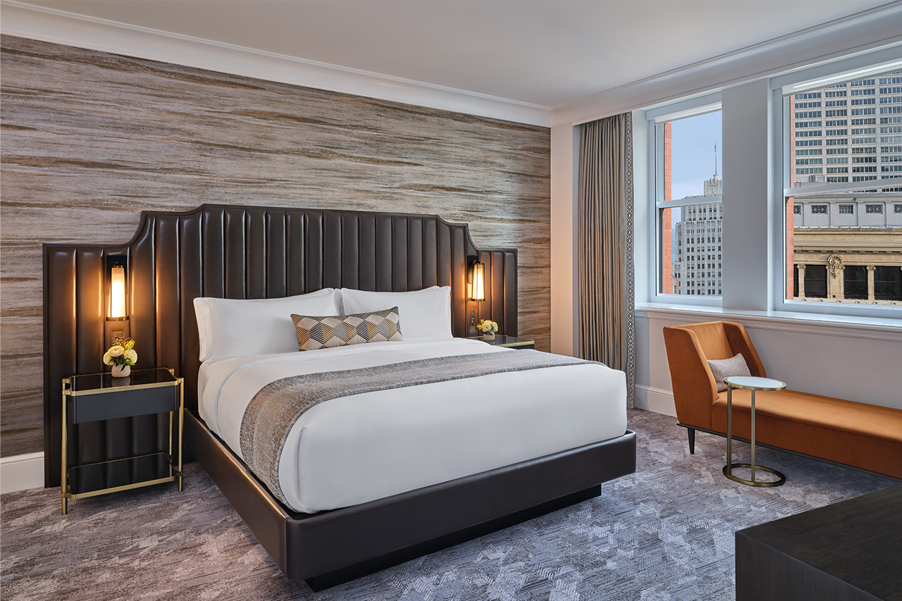 The Ritz-Carlton Club, San Francisco bedroom in a 2-bedroom residence. Furnished with a brown leather oversized headboard and bed, nightstands with lamps, orange chaise with side-table, and views of the city.